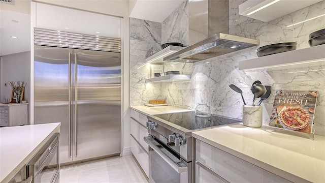 kitchen featuring light countertops, wall chimney range hood, backsplash, electric range oven, and stainless steel built in refrigerator