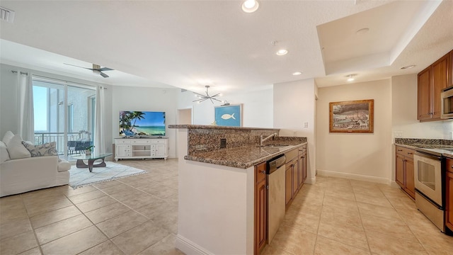 kitchen featuring open floor plan, dark stone countertops, appliances with stainless steel finishes, a peninsula, and brown cabinetry