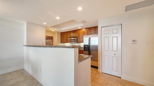 kitchen featuring visible vents, brown cabinets, dark stone countertops, appliances with stainless steel finishes, and a peninsula