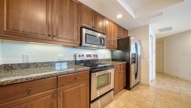 kitchen with visible vents, light tile patterned floors, dark stone countertops, brown cabinetry, and stainless steel appliances