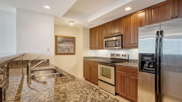 kitchen with brown cabinets, appliances with stainless steel finishes, dark stone counters, and a sink