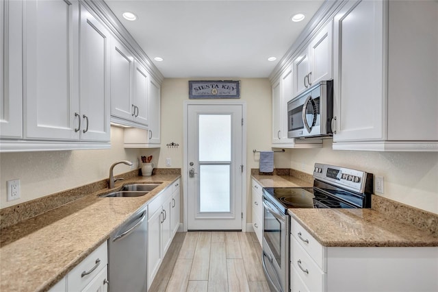 kitchen with stainless steel appliances, a sink, white cabinetry, and light wood-style floors