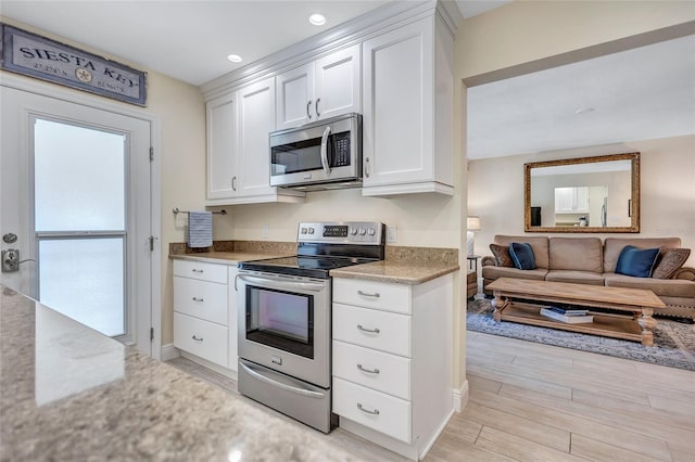 kitchen featuring open floor plan, appliances with stainless steel finishes, light wood-type flooring, and white cabinets