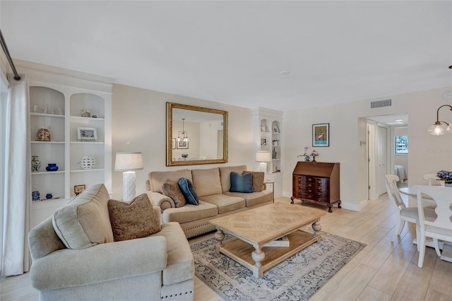 living room with built in features, light wood-type flooring, visible vents, and baseboards