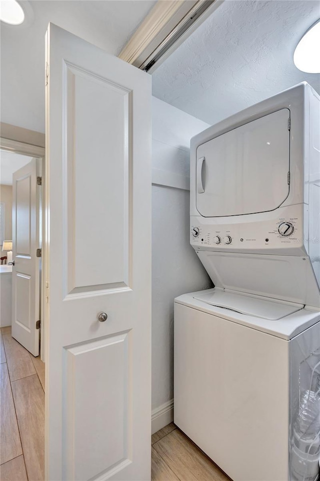 clothes washing area featuring laundry area, light wood finished floors, and stacked washer / dryer