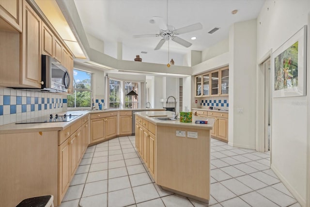 kitchen with light tile patterned floors, visible vents, light brown cabinetry, stainless steel microwave, and an island with sink