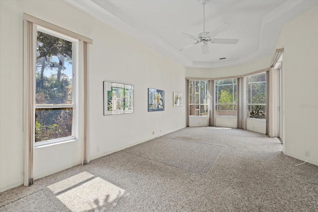 carpeted empty room featuring a raised ceiling, a healthy amount of sunlight, and ceiling fan