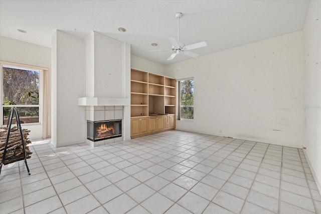 unfurnished living room with a ceiling fan, built in features, a tiled fireplace, and light tile patterned floors