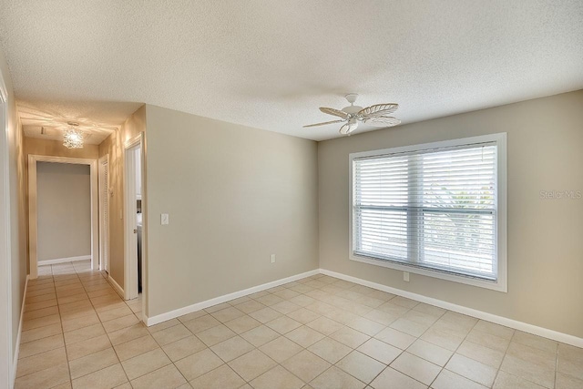 empty room with light tile patterned floors, ceiling fan, baseboards, and a textured ceiling