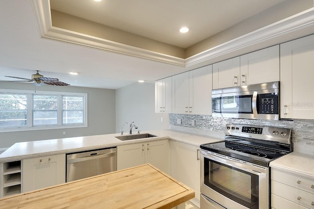 kitchen with stainless steel appliances, light countertops, backsplash, white cabinets, and a sink