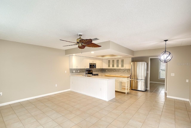 kitchen featuring decorative backsplash, glass insert cabinets, a peninsula, stainless steel appliances, and light countertops