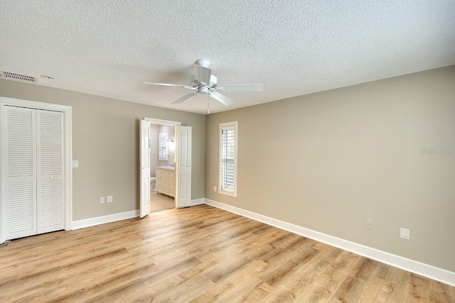 unfurnished bedroom with light wood finished floors, baseboards, visible vents, connected bathroom, and a textured ceiling