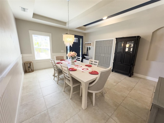 dining room with light tile patterned floors, visible vents, a raised ceiling, a wainscoted wall, and a decorative wall