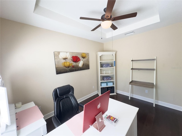 office area with visible vents, dark wood finished floors, baseboards, ceiling fan, and a tray ceiling