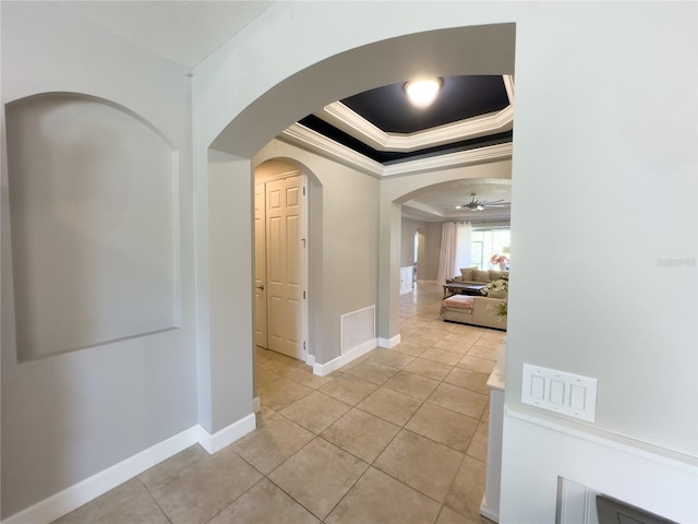 hall with light tile patterned floors, baseboards, a tray ceiling, and ornamental molding