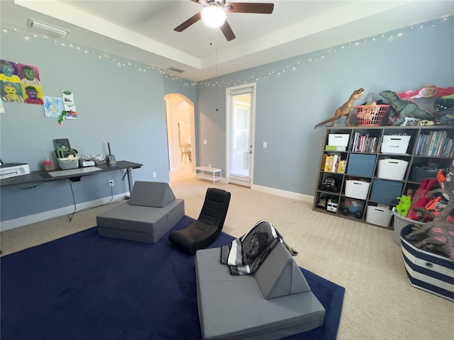 living area featuring baseboards, visible vents, arched walkways, a tray ceiling, and carpet flooring