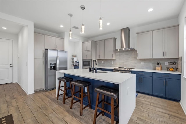 kitchen featuring stainless steel appliances, a sink, a kitchen breakfast bar, decorative backsplash, and wall chimney exhaust hood