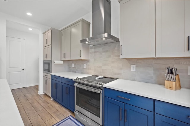 kitchen with decorative backsplash, wall chimney exhaust hood, appliances with stainless steel finishes, light countertops, and blue cabinetry