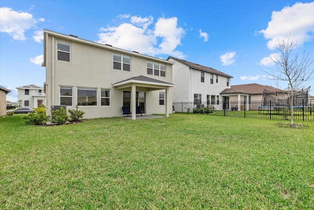 back of house featuring a lawn, a trampoline, fence, a patio area, and stucco siding