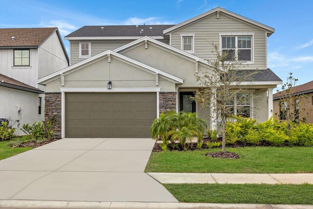 traditional home with roof with shingles, a front yard, a garage, concrete driveway, and stone siding