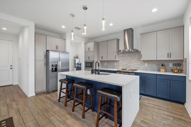 kitchen with a kitchen breakfast bar, appliances with stainless steel finishes, light wood-type flooring, a sink, and wall chimney exhaust hood