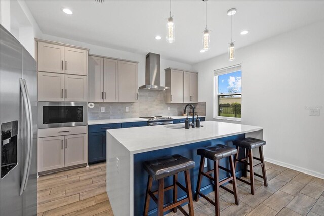 kitchen with stainless steel appliances, a sink, wall chimney exhaust hood, and light wood-style floors