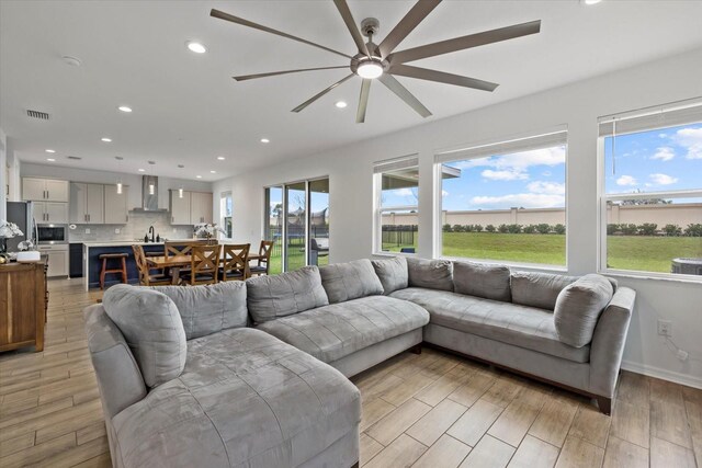 living room featuring a ceiling fan, visible vents, baseboards, light wood-style floors, and recessed lighting