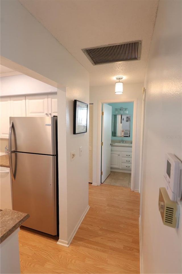 hall featuring visible vents, a sink, light wood-style flooring, and baseboards