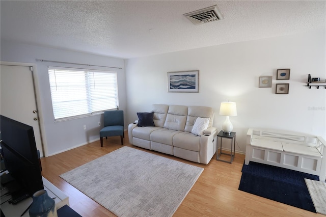 living room featuring a textured ceiling, light wood-style flooring, visible vents, and baseboards