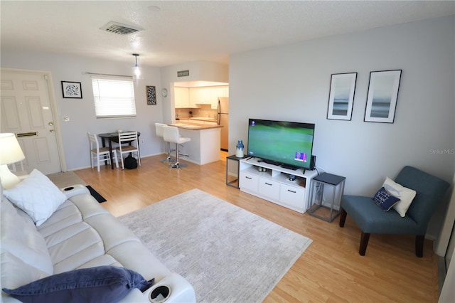 living room featuring a textured ceiling, light wood-style flooring, and visible vents