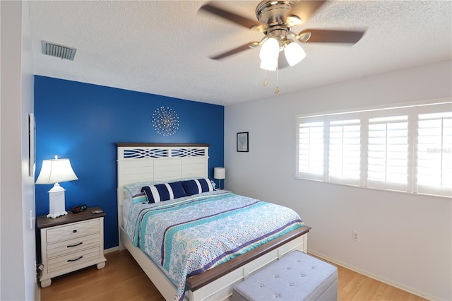 bedroom featuring a ceiling fan, visible vents, a textured ceiling, and light wood finished floors