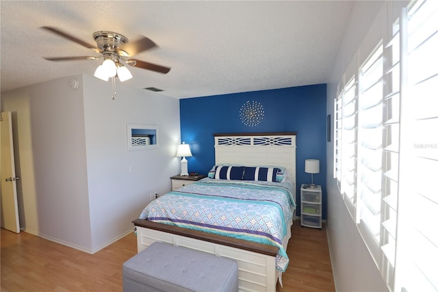 bedroom featuring baseboards, visible vents, ceiling fan, wood finished floors, and a textured ceiling