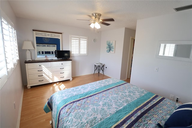 bedroom featuring light wood-type flooring, visible vents, ceiling fan, and a textured ceiling