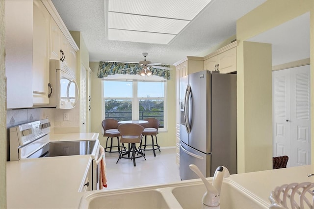 kitchen featuring light countertops, backsplash, a ceiling fan, a textured ceiling, and white appliances