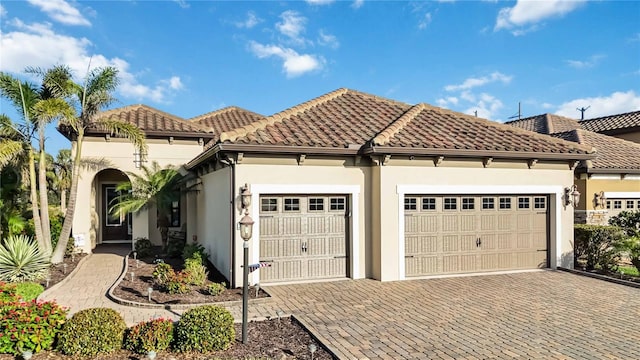 mediterranean / spanish house featuring a garage, a tiled roof, decorative driveway, and stucco siding