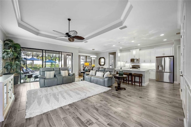 living area featuring light wood finished floors, visible vents, ceiling fan, and a tray ceiling