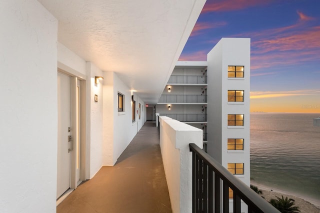 corridor featuring concrete floors, a water view, and an upstairs landing