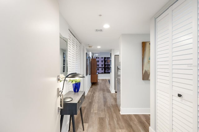 hallway with light wood finished floors, baseboards, visible vents, and recessed lighting