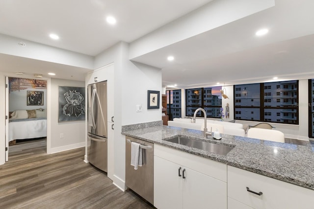 kitchen with white cabinets, appliances with stainless steel finishes, dark wood-type flooring, light stone countertops, and a sink