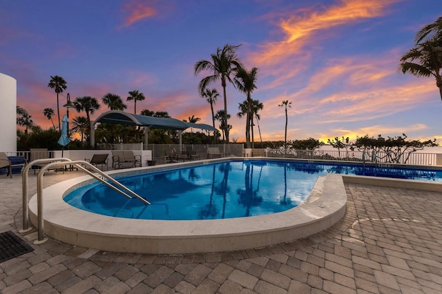 pool at dusk featuring a patio area, a community pool, and fence