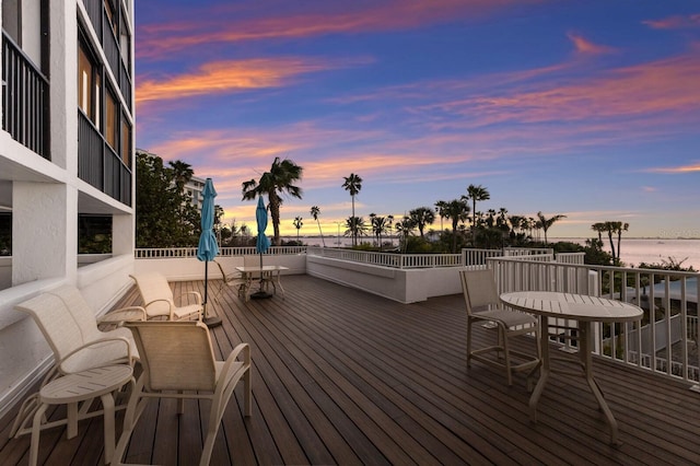 deck at dusk with outdoor dining area and a water view