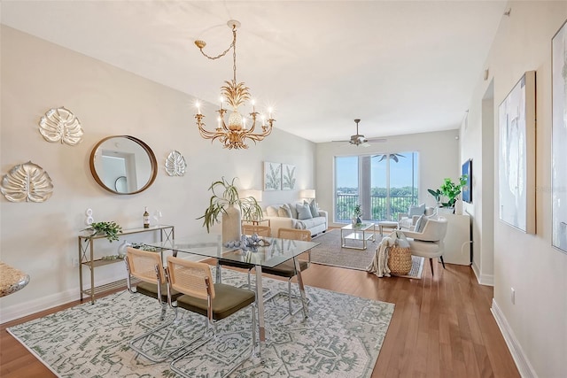 dining space with ceiling fan with notable chandelier, baseboards, and wood finished floors