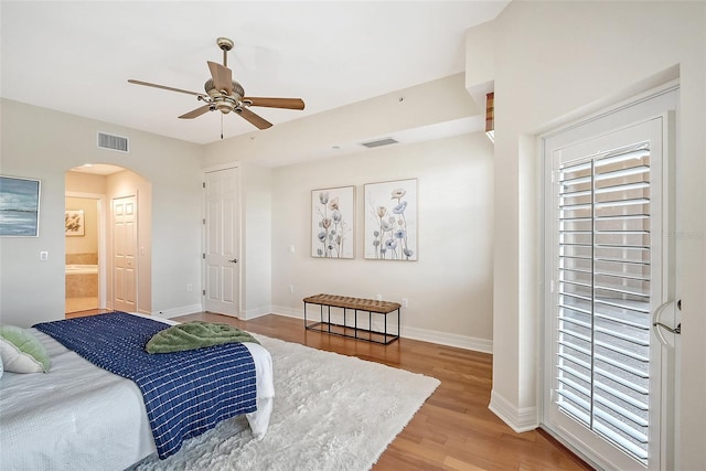 bedroom with arched walkways, light wood finished floors, visible vents, and baseboards