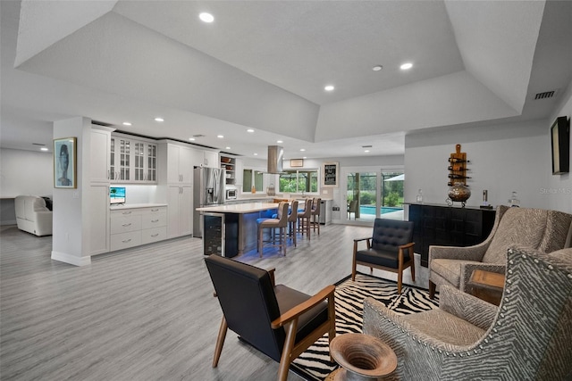 living area with a raised ceiling, recessed lighting, light wood-style floors, and visible vents