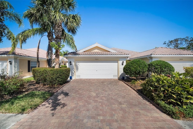 view of front facade with a garage, decorative driveway, a tile roof, and stucco siding