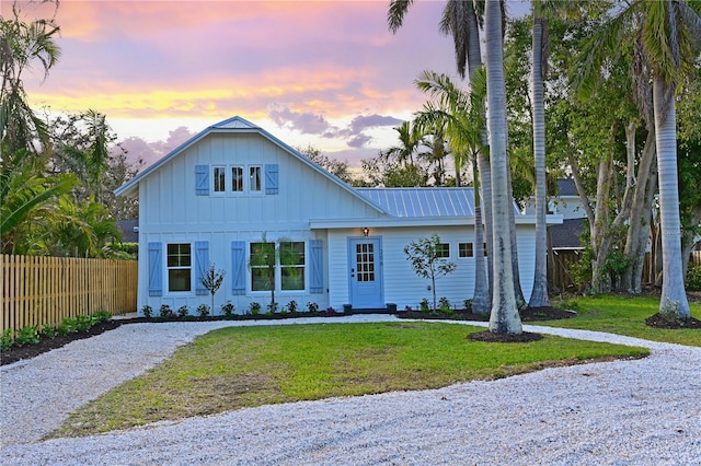 modern farmhouse with metal roof, fence, driveway, a lawn, and board and batten siding