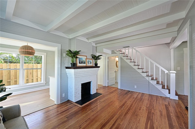 unfurnished living room with hardwood / wood-style flooring, a fireplace, beamed ceiling, and stairs