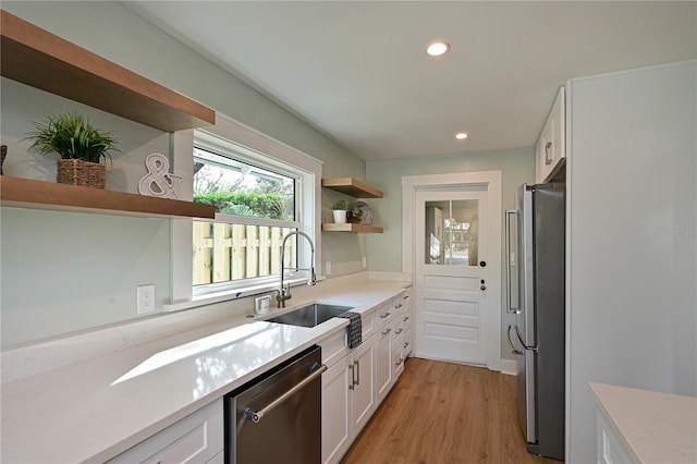 kitchen with stainless steel appliances, a sink, white cabinetry, light countertops, and open shelves