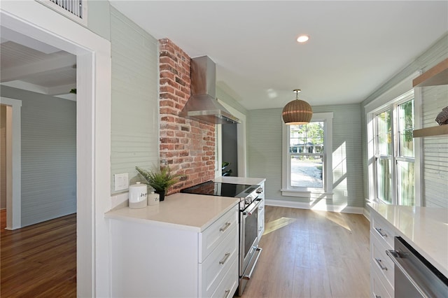 kitchen with stainless steel appliances, wall chimney exhaust hood, light countertops, and white cabinetry