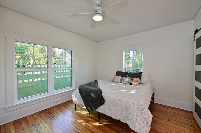 bedroom with hardwood / wood-style floors, a barn door, a ceiling fan, and baseboards